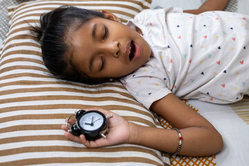 Child sleeping peacefully with alarm clock by side