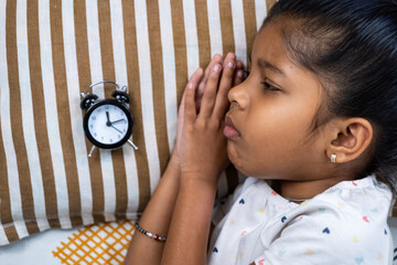 Girl waiting anxiously beside alarm clock on bed