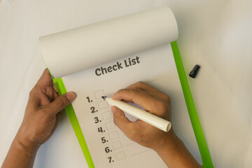 Top view of a hand marking a checklist on a notepad with a green cover and a marker pen. Person...