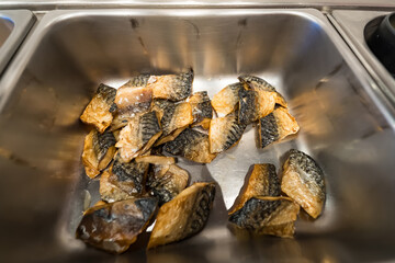 Pieces of cooked salmon with skin are displayed in a stainless steel tray at a buffet serving station in a restaurant kitchen