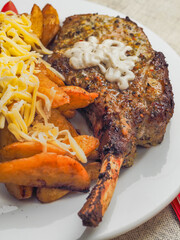 A plate of food with a premium pork chop in the bone, wedges potatoes, and tomatoes and cheddar...