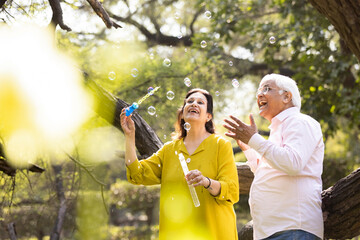 Active senior couple having fun blowing bubbles at park