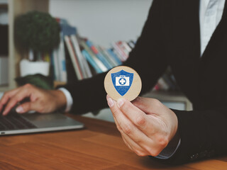 Health insurance concept with person holding medical symbol shield and laptop on wooden table in office environment