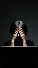 A person displaying signs of stress and frustration while working on a laptop in a dimly lit space.