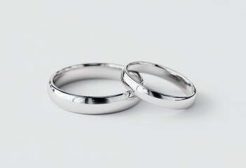 Two simple, smooth, silver wedding bands lie side-by-side on a light gray background