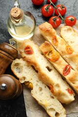Pieces of delicious focaccia with tomatoes, spices and oil on dark table, flat lay