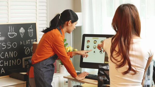 A young Asian female barista in modern cafe assists woman customer ordering latte, fresh coffee beans, dark roast, croissant, completing the purchase with mobile payment at the POS using QR code.