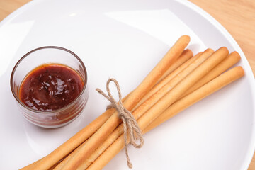pack of breadsticks with ketchup dipping sauce in white dish on wood table