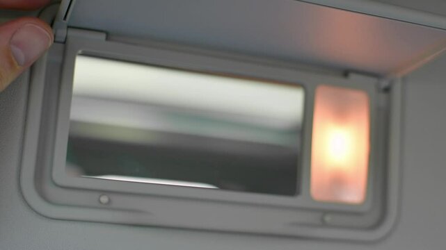 Hand gently closes sun visor mirror in car, turning off integrated light and highlighting smart interior design and comfort features.