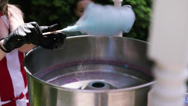 Seller Makes Cotton Candy, a Machine for Making Cotton Candy on the Street. The process of making an airy blue cloud from sugar for cotton candy in the park. Children's party. Selling street sweets.