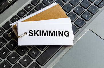 Skimming text on white notepad with laptop keyboard background. Hacker and scam activity concept