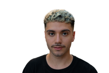 A young man with short curly bleached hair, a septum piercing, and light stubble looks confidently at the camera, wearing a black shirt against a dark background.
