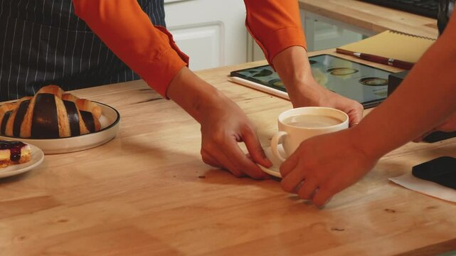 A young Asian female barista in modern cafe assists woman customer ordering latte, fresh coffee beans, dark roast, croissant, completing the purchase with mobile payment at the POS using QR code.