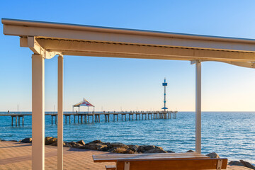 Brighton Jetty with people viewed from Esplanade through picnic gazebo on a bright day, Adelaide, South Australia
