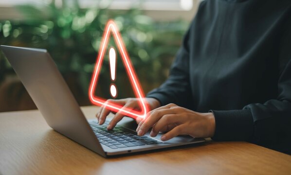 Person using laptop with warning sign alert online security risk