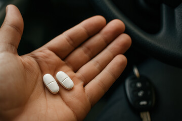 Hand holding two white tablets with car keys in background, highlighting medication and safe driving awareness