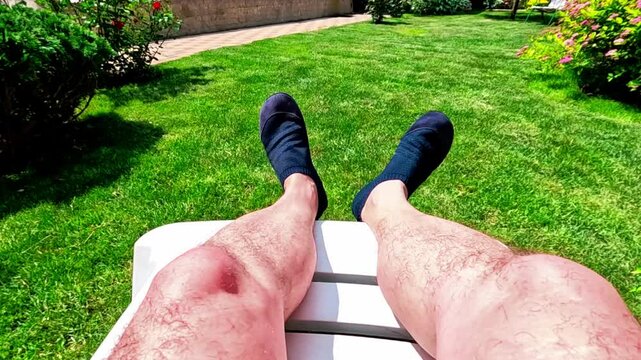 Closeup hairy male legs on plastic deck chair in the garden 