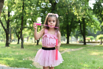 Child is playing with soap bubbles in the park.
