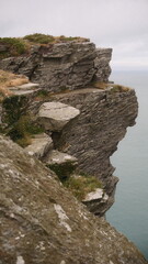 A man standing on top of a cliff next to a body of water the scene features  under moody and dramatic conditions.