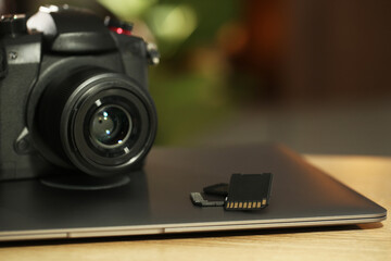 SD memory cards, laptop and photo camera on wooden table, closeup