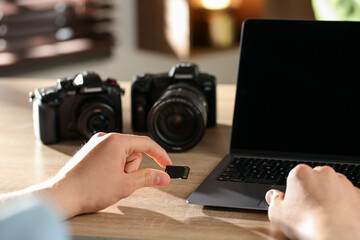 Man inserting SD memory card into laptop at wooden table indoors, closeup