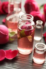 Open perfume bottles with aromatic essential oils and roses on grey wooden table, closeup
