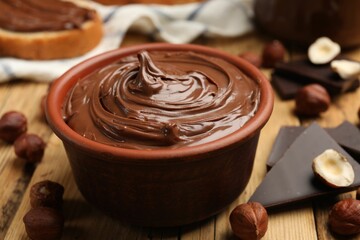 Tasty hazelnut spread, chocolate pieces and nuts on wooden table, closeup