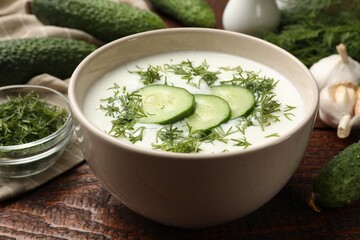 Tasty cucumber soup in bowl and ingredients on wooden table, closeup