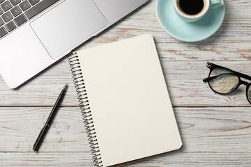 Notebook with pen, laptop, glasses and coffee on white wooden table, flat lay
