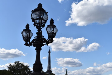 Lampadaire à trois lampes sous un ciel bleu, face à la Tour Eiffel.