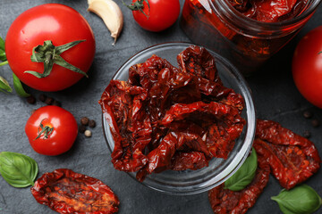Tasty sun dried tomatoes, fresh vegetables and peppercorns on black table, flat lay