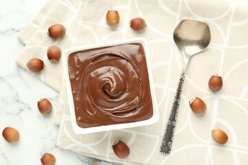 Tasty chocolate spread and hazelnuts on white table, flat lay