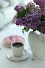 Bouquet of beautiful lilac flowers, coffee and dessert on white table indoors