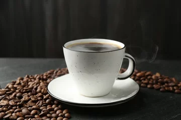 Aromatic coffee in cup and beans on black table, closeup