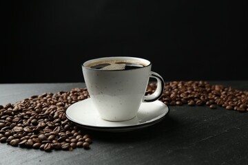 Aromatic coffee in cup and beans on black table, closeup