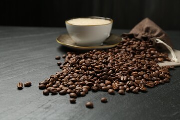 Aromatic coffee beans and hot drink on black table, closeup