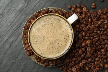 Aromatic coffee in cup and beans on black table, flat lay