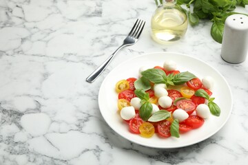 Tasty salad with mozzarella, tomatoes and basil served on white marble table. Space for text