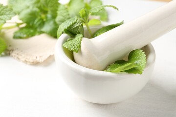 Fresh lemon balm leaves and pestle in mortar on white wooden table, closeup