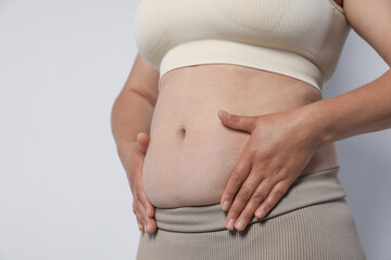 Woman with excessive belly fat on light background, closeup. Overweight problem