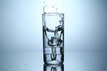 Fresh water splashing out of glass on mirror table against light grey gradient background, closeup