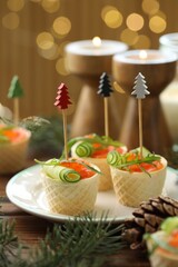 Tasty canapes and festive decor on wooden table against blurred lights, closeup. Bokeh effect
