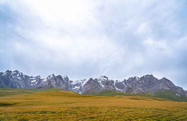 An expansive view of golden and green grasslands stretching towards a horizon dominated by rugged,...
