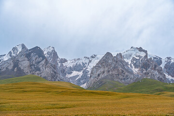 A wide view of a grand mountain range featuring snow-dusted peaks and rocky formations, rising...