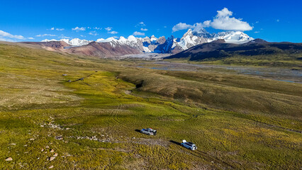 An aerial shot of off-road vehicles traversing a vast, green and brown mountain tundra, with...