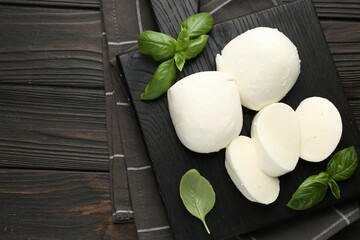 Pieces of delicious mozzarella cheese and basil on wooden table, top view. Space for text