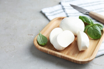 Pieces of delicious mozzarella cheese and basil leaves on grey textured table, closeup. Space for text