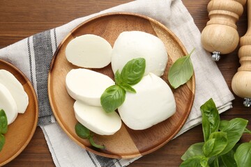 Pieces of delicious mozzarella cheese, basil leaves and shakers on wooden table, flat lay