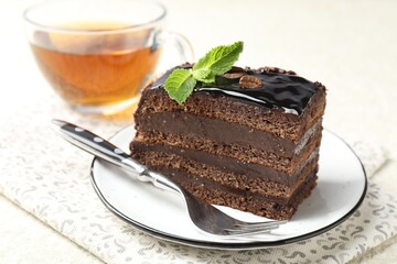 Piece of chocolate cake served with mint, fork and tea on white table, closeup