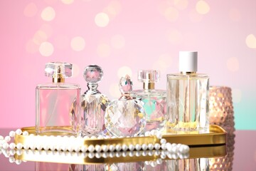 Many different perfume bottles and accessories on mirror surface against pink background with...